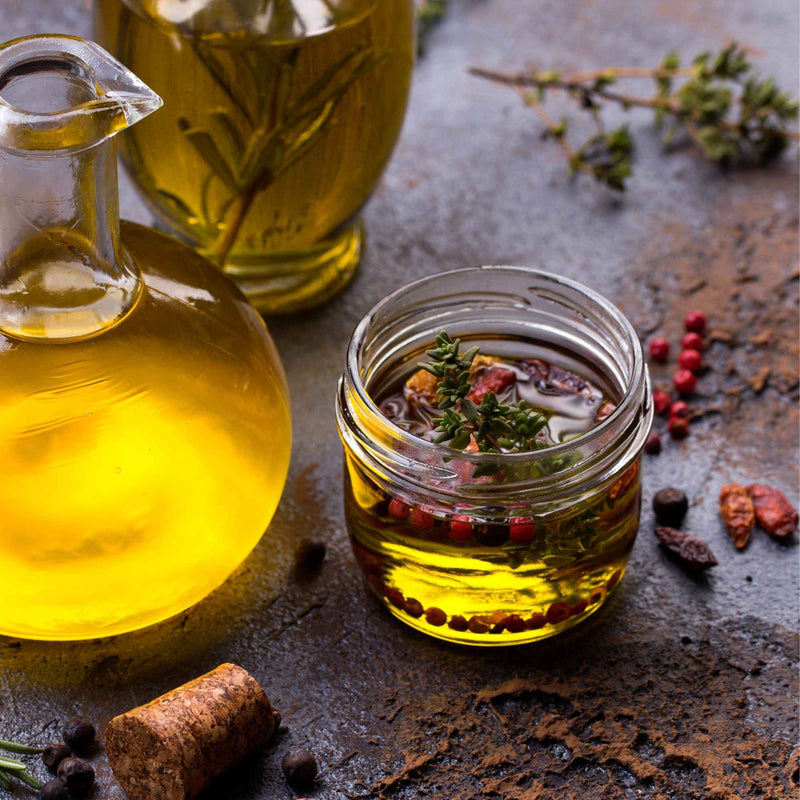 Petit pot d’huile d’olive infusée aux herbes et aux baies, à côté d’une carafe.