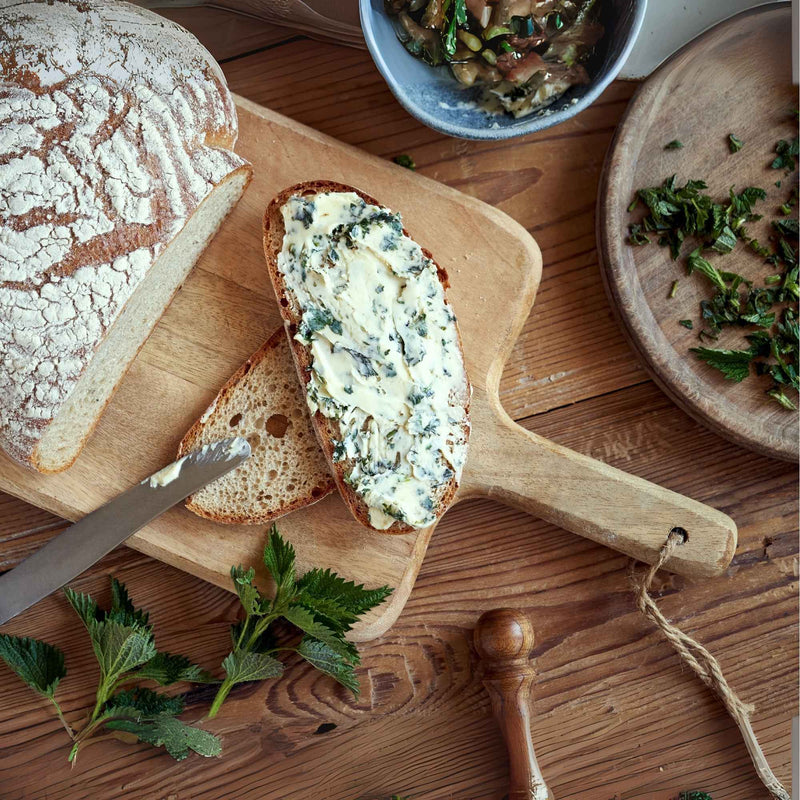 Tranche de pain tartinée de beurre à l’ortie fait maison sur une planche en bois.