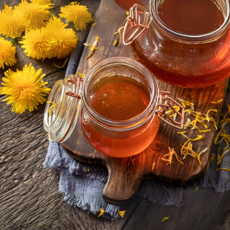 Bocal de sirop de pissenlit fait maison entouré de fleurs jaunes fraîches.