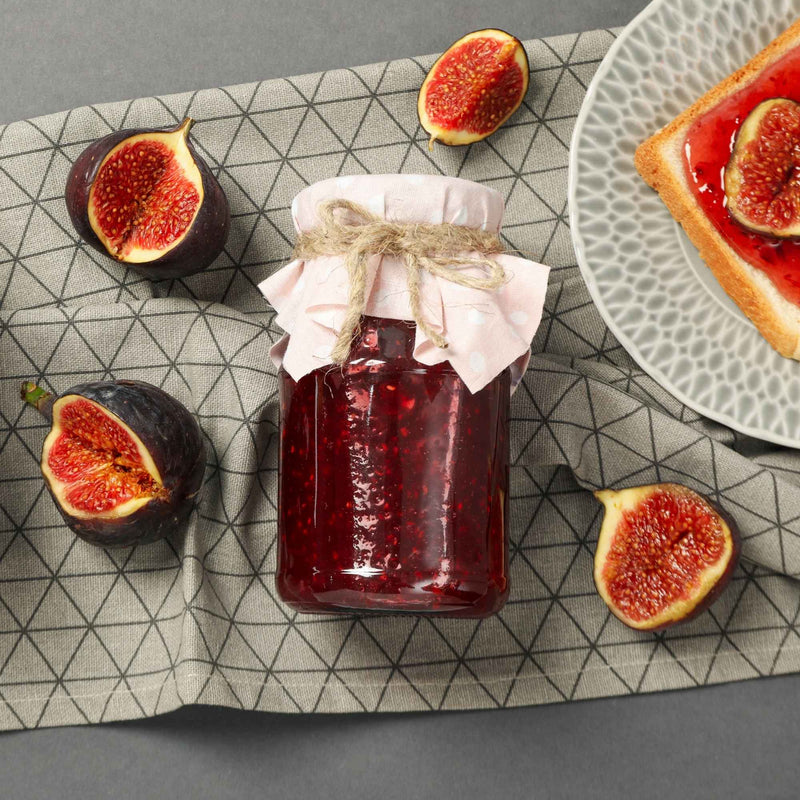 Pot de confiture aux figues maison, entouré de figues fraîches et d’une tartine.