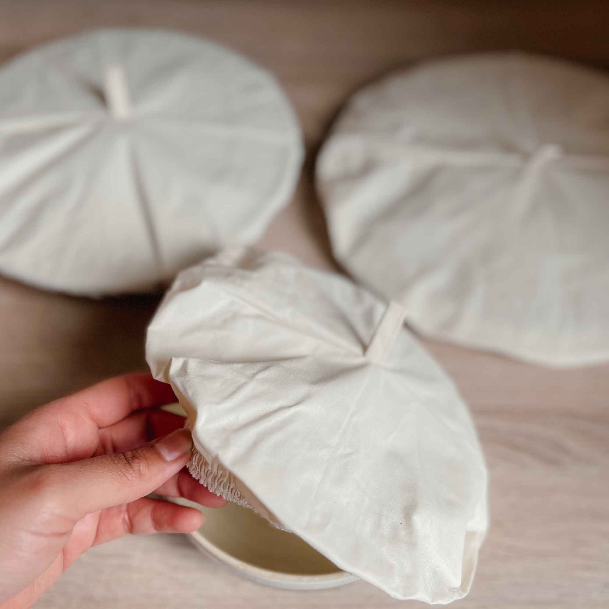 Gros plan d’un couvercle en coton bio tenu à la main, pratique et ajustable pour recouvrir bols et plats.