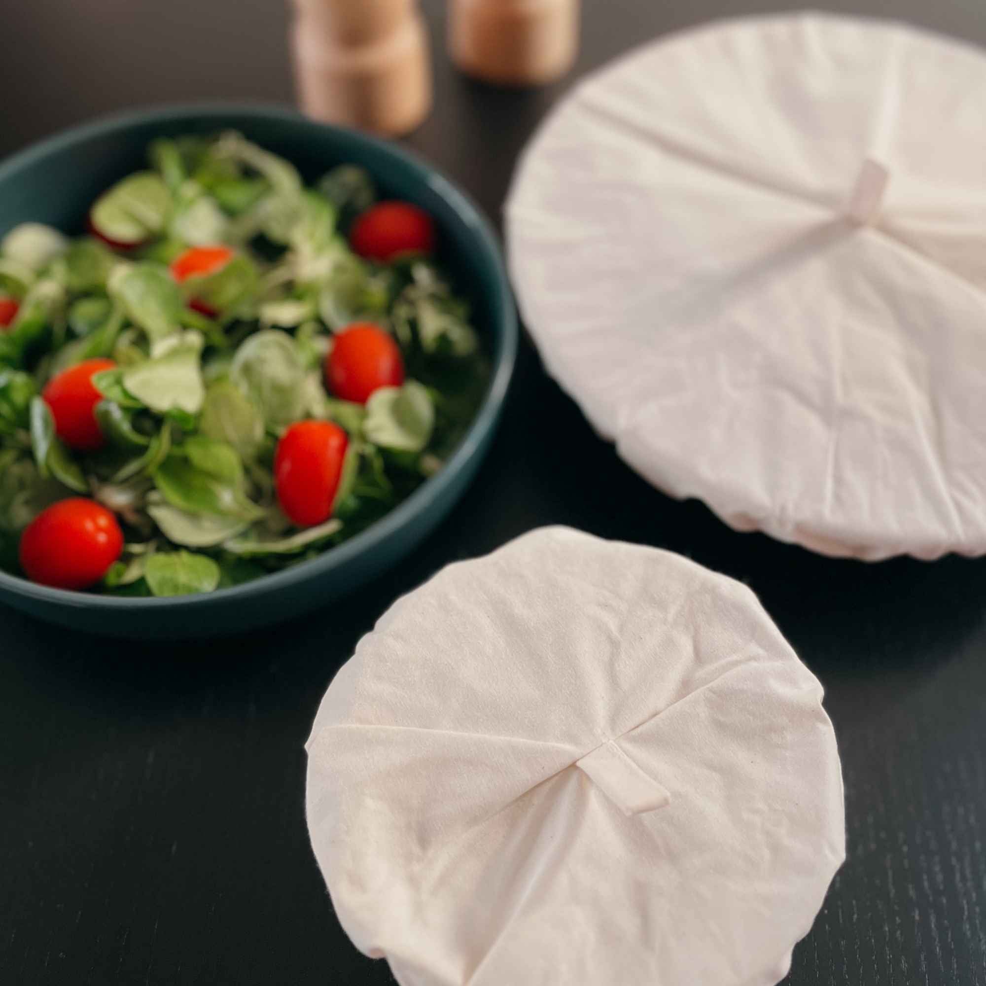 Couvercles en coton bio posés près d’un bol de salade et tomates, pour conserver les aliments de manière naturelle.