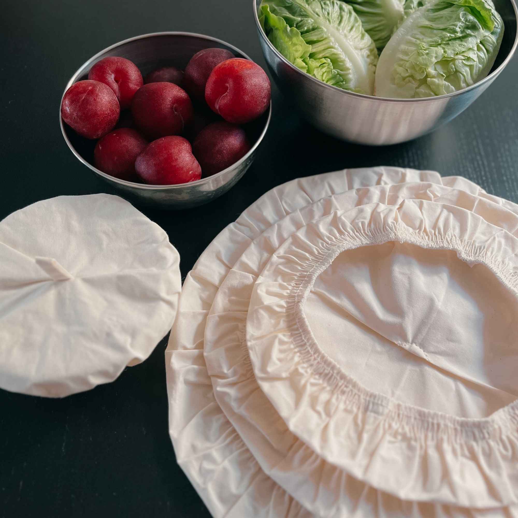 Ensemble de couvercles en coton bio de différentes tailles, posés sur une table avec fruits et légumes frais.