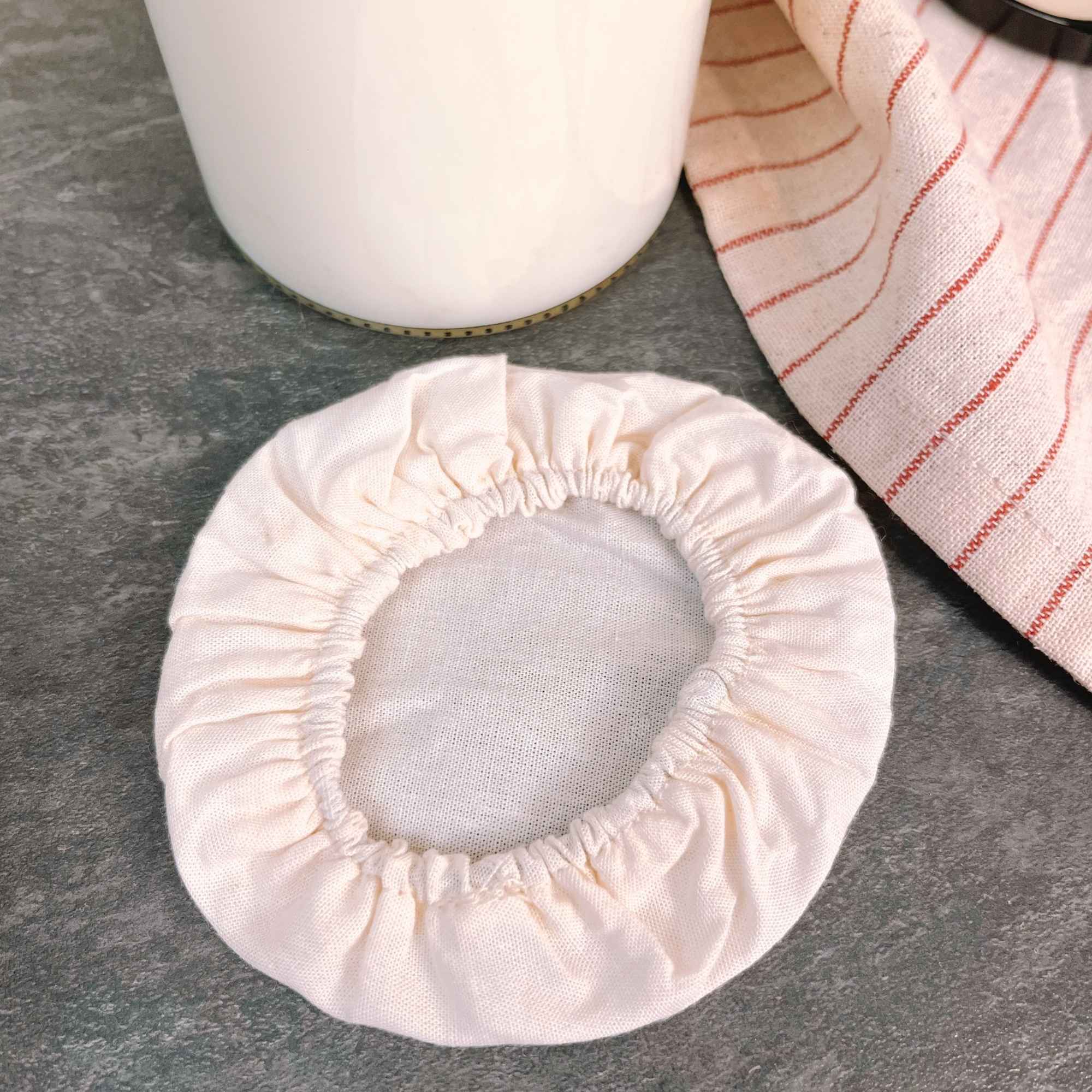 Bocal de kéfir de lait recouvert d’un couvre-pot en tissu, fermentation maison protégée et aérée.